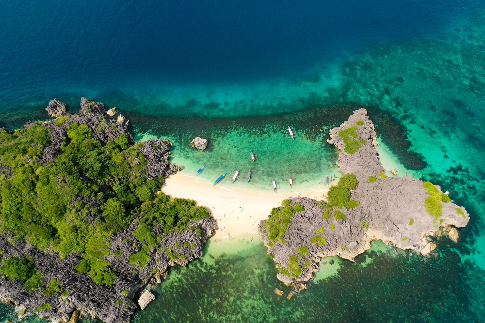 Top view of small tropical island with white sandy beach and blue transparent water. Lahos Island, Caramoan Islands, Philippines.